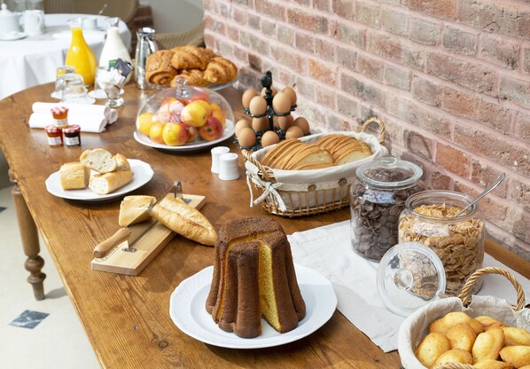 A breakfast buffet with bread, pastries, fruits, eggs, and cereals on a wooden table. - Hôtel Jean de Bruges (Saint-Riquier)