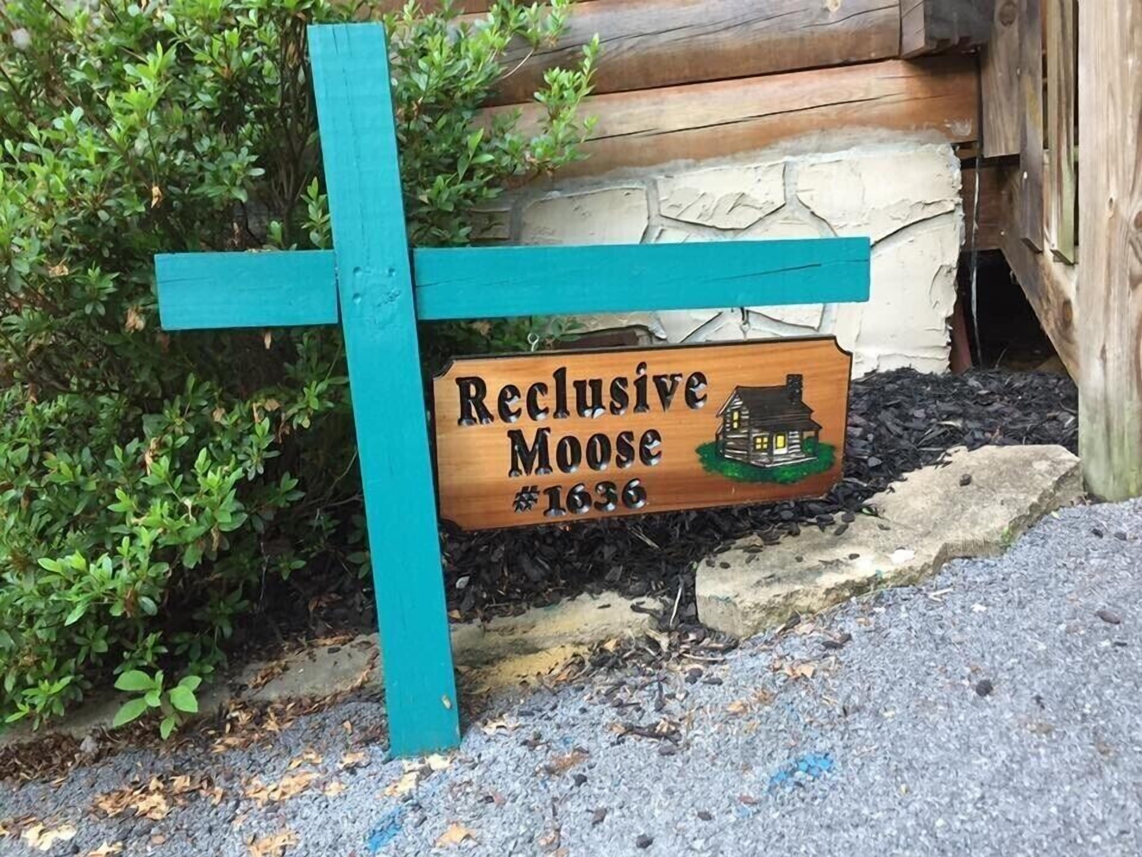 Un panneau en bois, orné d’une illustration représentant une maison et portant l’inscription « Reclusive Moose #1636 », est fixé sur un poteau de couleur turquoise.