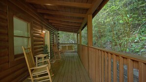 A wooden cabin with a covered porch, rocking chairs, and a view of the surrounding forest. - Cozy cabin, perfect for a honeymoon or an adventure-filled family getaway! (Gatlinburg)