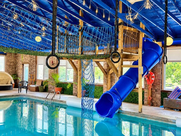 An indoor swimming pool with a slide, rope net, and wooden play structures.