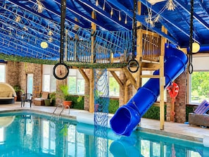 Una piscina interior con tobogán, red de cuerdas y juegos de madera.