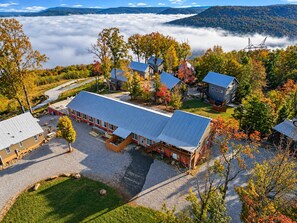 A large building with a flat roof, surrounded by trees with autumn foliage, and a mountainous backdrop.