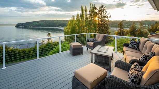 Een terras met rieten meubilair, een tafel en uitzicht op een meer en bos.