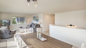 Een moderne woonkamer met een houten eettafel, een grijze bank en een televisie op een dressoir.