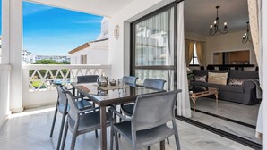 A balcony with a dining table and chairs, a view of the city, and a living area with a sofa and a coffee table. - Beachfron Puerto Banus, 2 bed apt Playas Del Duque, Free Wifiparking 3 Pools (Marbella)