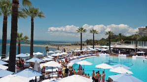 A poolside area with lounge chairs and umbrellas, palm trees, and a view of the beach and ocean. - Beachfron Puerto Banus, 2 bed apt Playas Del Duque, Free Wifiparking 3 Pools (Marbella)