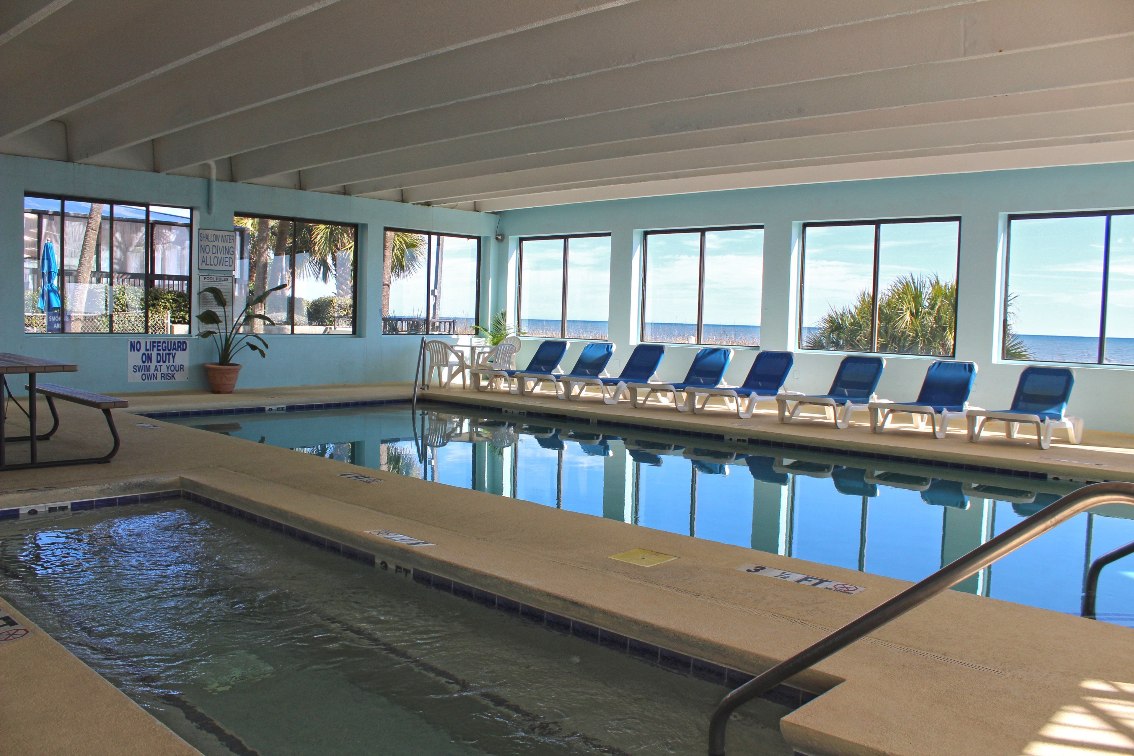 An indoor swimming pool with clear blue water, a lifeguard station, and lounge chairs facing the pool.