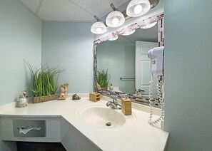 Un baño con un lavamanos blanco, un espejo grande con iluminación y plantas decorativas.