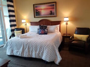 Habitación de hotel con una cama grande, dos lámparas de noche, un cabecero de madera y un cuadro de un atardecer.