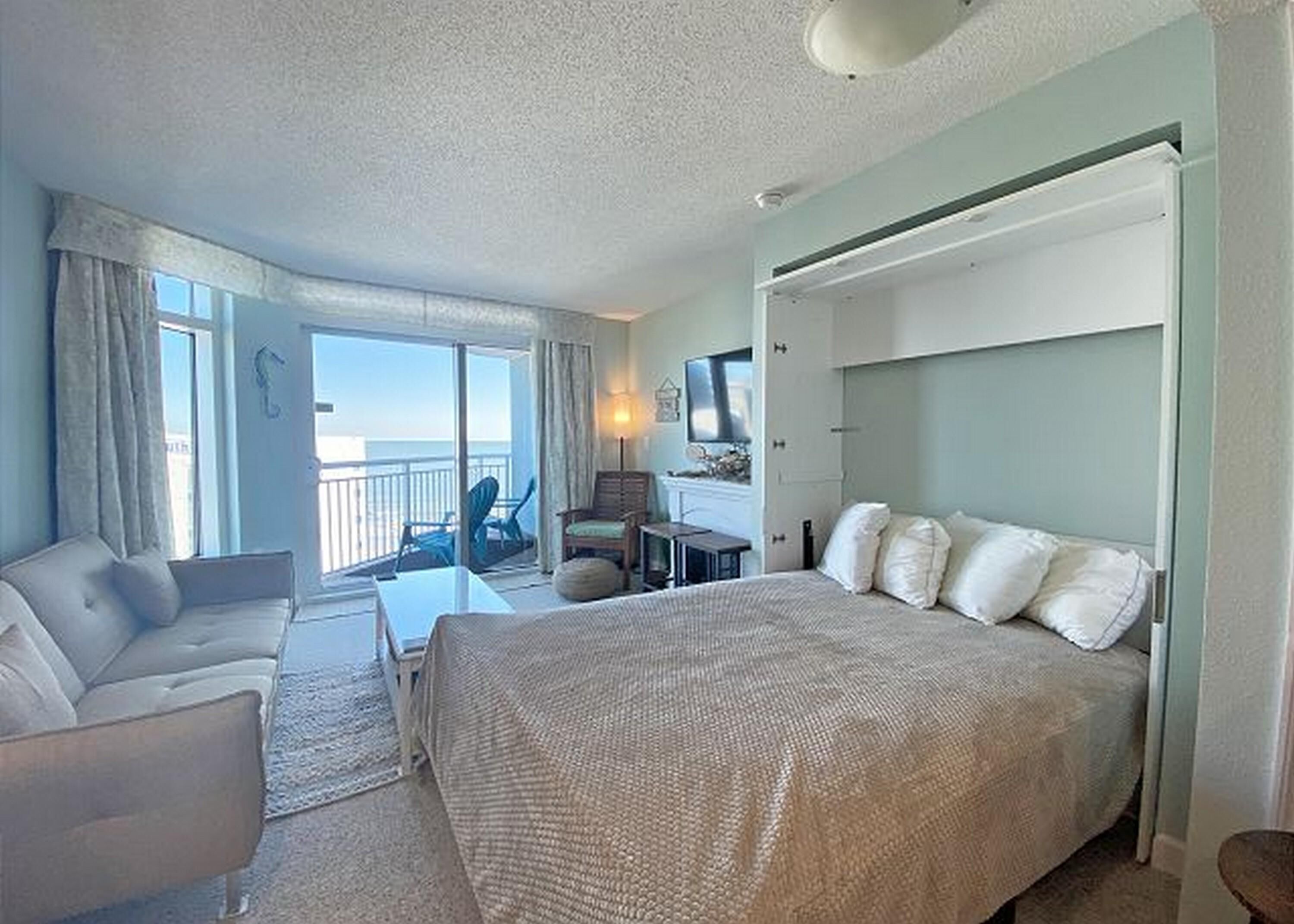 A hotel room with a large bed, a sofa, a desk, and a view of the sea.