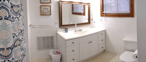 A bathroom with a white vanity, a mirror, a toilet, and patterned curtains.