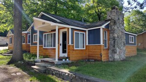 Une cabane en rondins avec une cheminée en pierre, une véranda et un petit jardin devant.