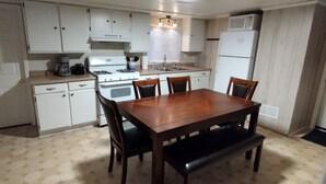 Une cuisine compacte avec des meubles blancs, une cuisinière et un four à micro-ondes. On y trouve une table à manger en bois et quatre chaises.