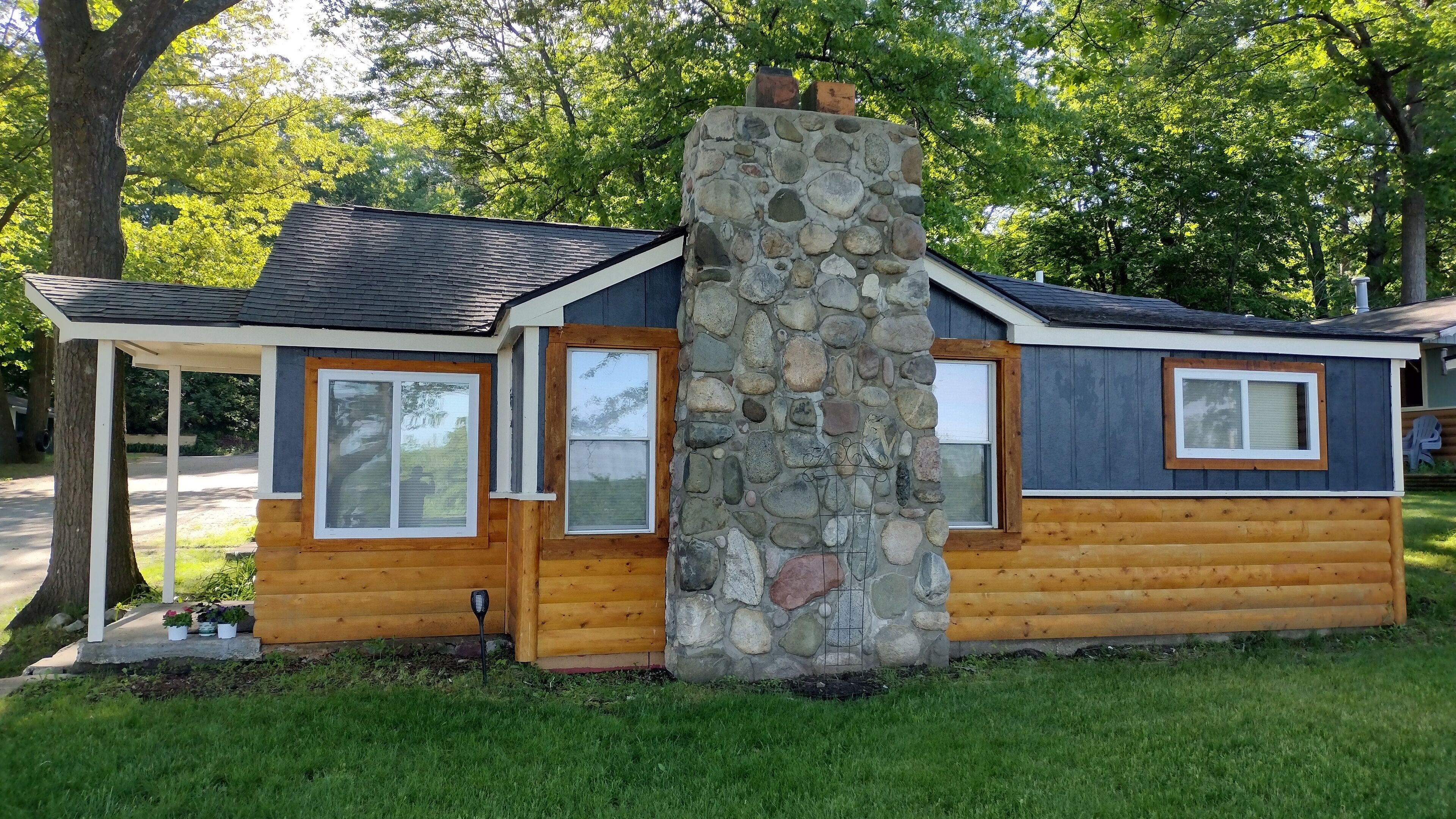 A log cabin with a stone chimney, wooden exterior, and two windows.