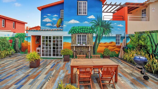 Ein farbenfrohes Haus mit Wandgemälde, einer Holzterrasse, einem Grill und Sitzgelegenheiten im Freien.