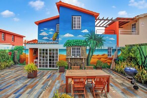 A colorful house with a mural, a wooden deck, a barbecue grill, and outdoor seating. - This Villa is Ideal for Families With Children (La Oliva)