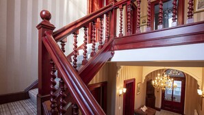 A grand staircase with a wooden handrail and balusters, leading to a second-floor landing with a chandelier and a cowhide rug. - Newton Manor House -7 Bedroom House (Cupar)