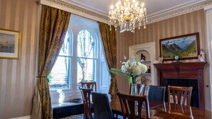 A dining room with a chandelier, wooden chairs, a table, a fireplace, and a window with curtains. - Newton Manor House -7 Bedroom House (Cupar)