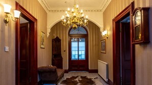 A hallway with a chandelier, a red door, a brown leather chair, and a cowhide rug. - Newton Manor House -7 Bedroom House (Cupar)