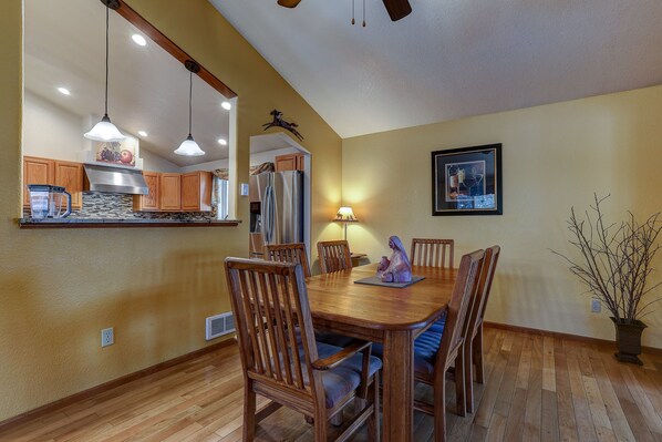 A dining area with wooden chairs and a table, a kitchen with wooden cabinets and a refrigerator, and a framed picture on the wall. - Larkspur Trail 3 Bedroom Home by RedAwning (Bend)