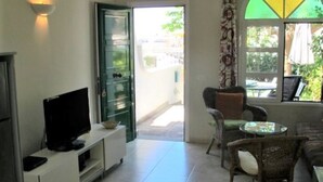 Ένα σαλόνι με τηλεόραση, έναν καναπέ, ένα τραπέζι φαγητού και ένα παράθυρο με θέα προς τα έξω.