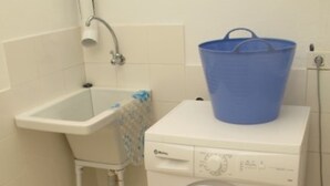Ένας μικρός, λειτουργικός χώρος πλυντηρίου με ένα πλυντήριο ρούχων και έναν νιπτήρα.