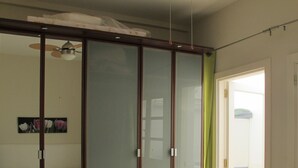 Ένα υπνοδωμάτιο με συρόμενη γυάλινη πόρτα, ένα κρεβάτι με ένα διακοσμητικό κάλυ μμα με σχέδια λουλουδιών και έναν ανεμιστήρα οροφής.