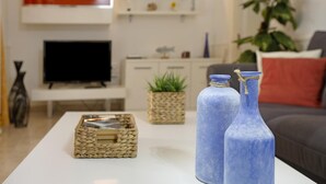 Een moderne woonkamer met een witte salontafel, twee blauwe vazen, een geweven mand, een flatscreen-tv en een bank met rode kussens.