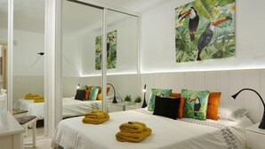 Een hotelkamer met een groot bed, twee nachtkastjes, een spiegel en een tropisch schilderij aan de muur.