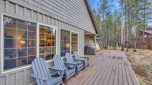 A wooden deck with Adirondack chairs, a covered grill, and a view of a forested area. - Gosling Lane 6 (Bend)