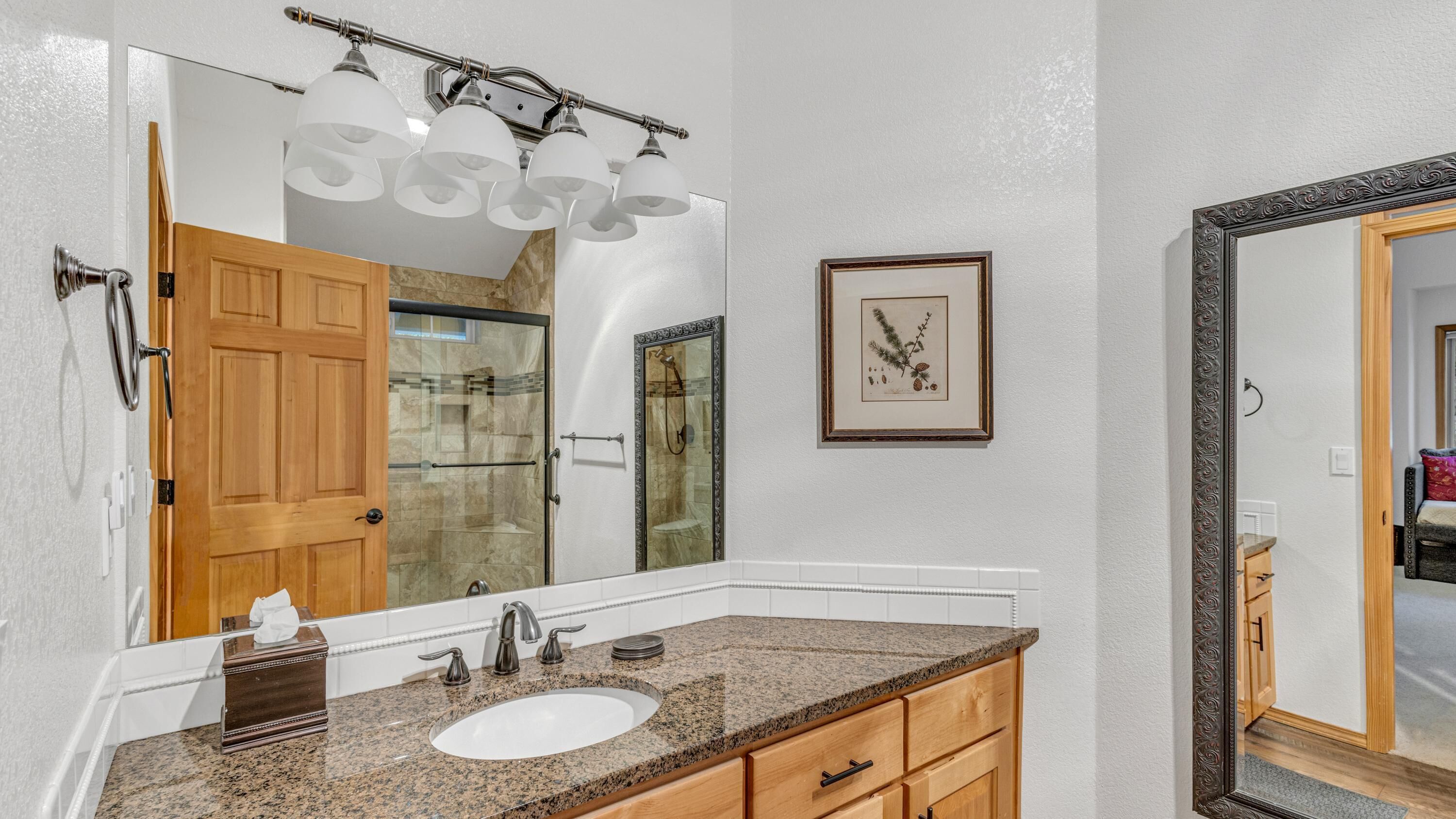 A bathroom with a granite countertop sink, a large mirror, and a shower with a glass door.