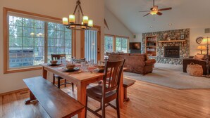 A spacious living room with a fireplace, a dining area with a wooden table and benches, and a ceiling fan. - Gosling Lane 6 (Bend)