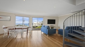 Relax in a spacious living area with a dining table, sofa, and TV, offering a balcony with a sea view.