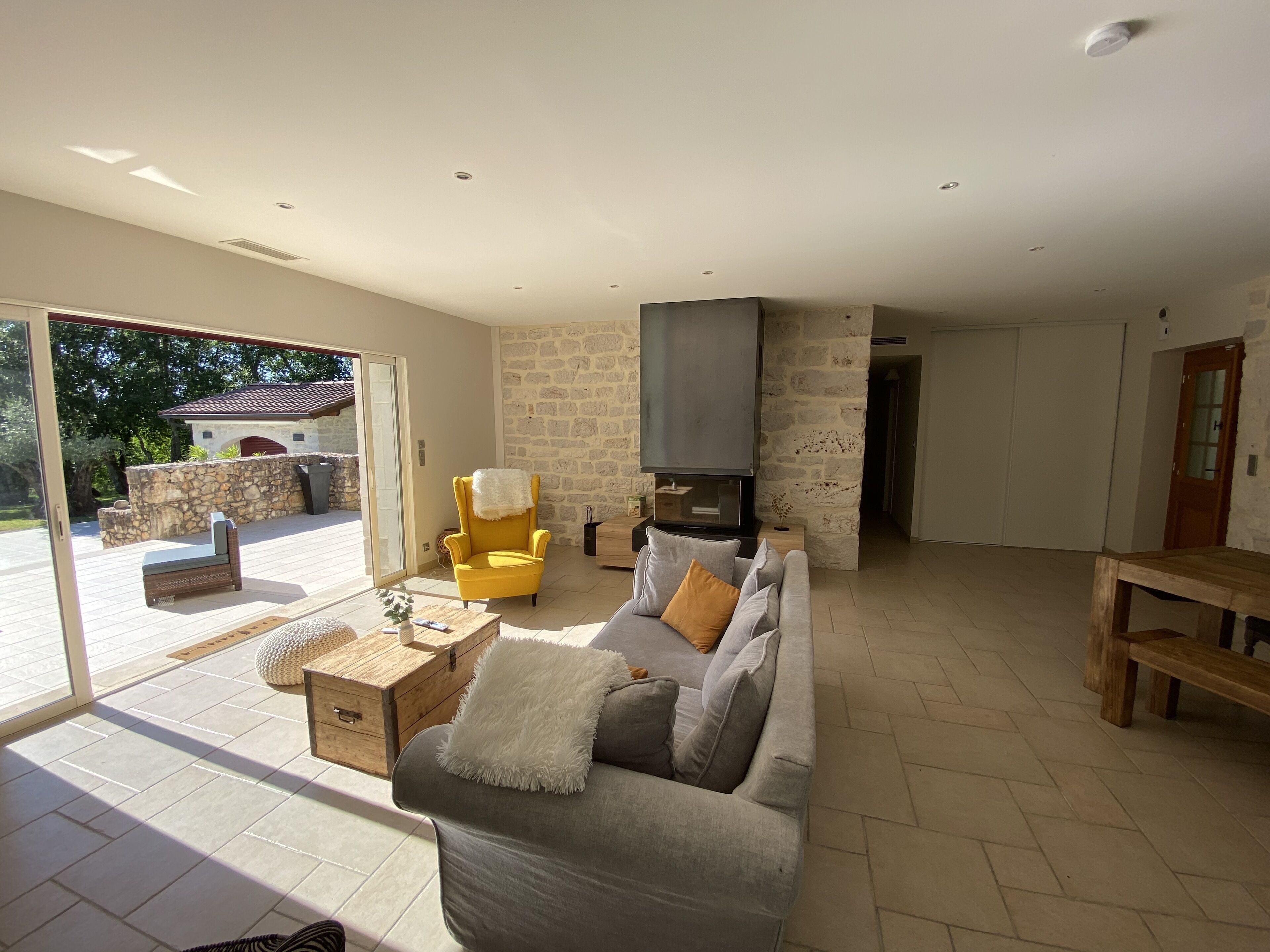 A spacious living room with a grey sofa, yellow armchair, and a fireplace.