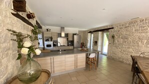 A modern kitchen with a central island, stone walls, and a dining area with wooden furniture. - The butterflies of Quercy (Caylus)