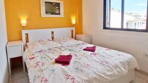 Een slaapkamer met een bed, twee nachtkastjes, een plafondventilator, een raam en een aan de muur bevestigd schilderij.