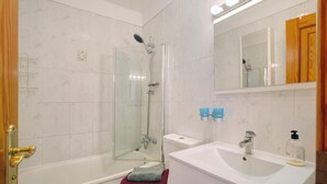 Een badkamer met een douche met glazen wand, een witte wastafel en een spiegel erboven.