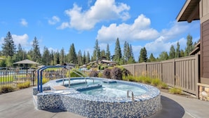 A hot tub with mosaic tile design, surrounded by a wooden deck and a stone wall. - Ollalie Lane 7 (Bend)