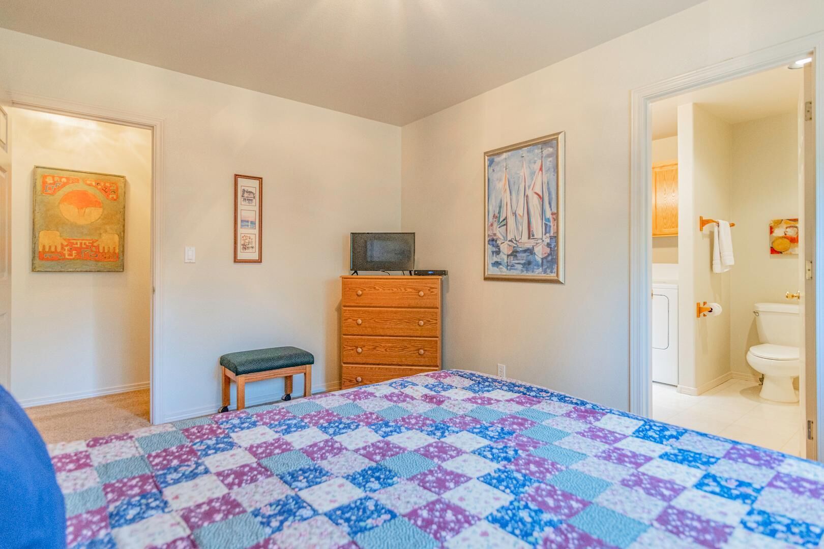 A bedroom with a bed, dresser, and artwork on the walls.