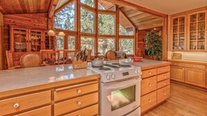 A spacious kitchen with wooden cabinets, a large island with a stove, and ample natural light from large windows. - Wood Duck Drive 55905 (Bend)