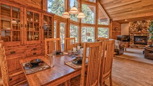 A wooden cabin interior with a dining area, stone fireplace, and large windows. - Wood Duck Drive 55905 (Bend)