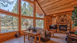 A spacious living room with large windows, a stone fireplace, and a cozy seating area. - Wood Duck Drive 55905 (Bend)