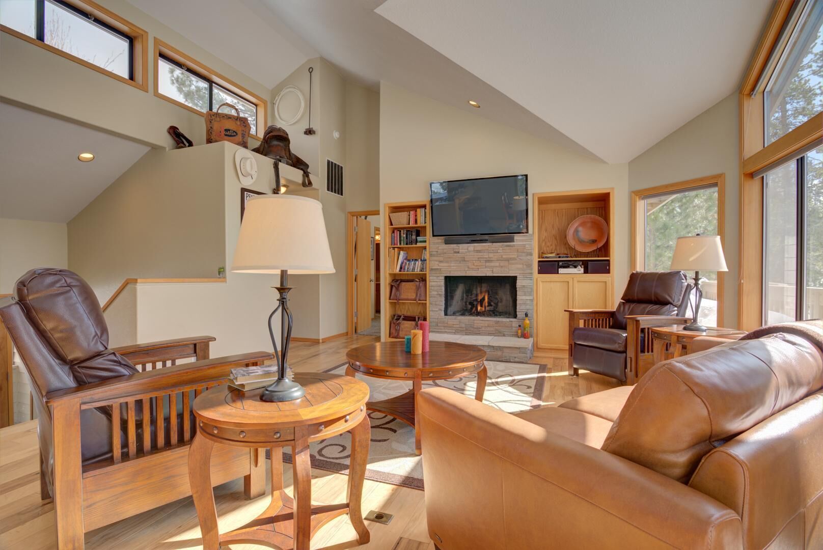 Amplia sala de estar con muebles de cuero, chimenea, televisor y ventanas grandes.