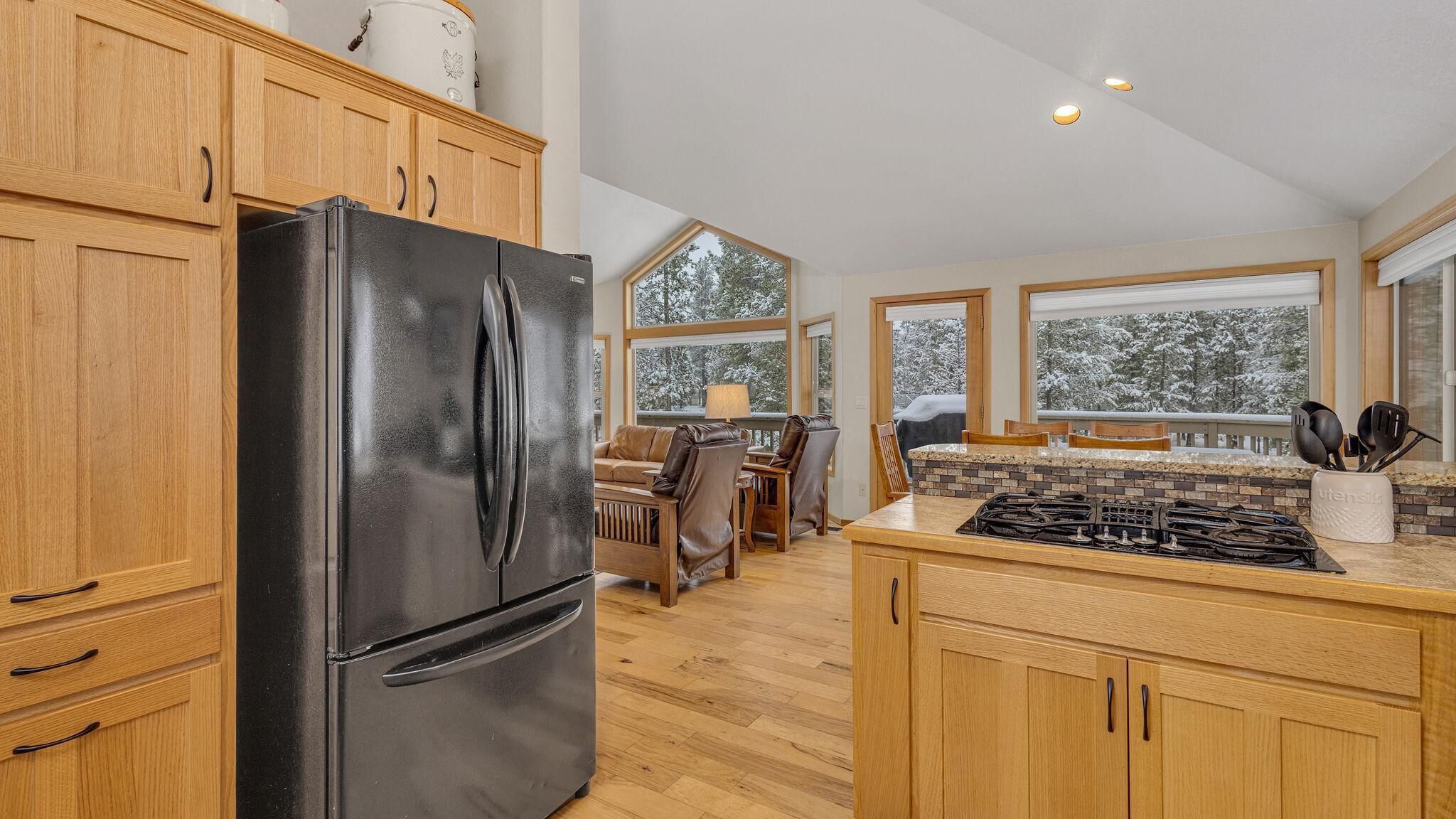A kitchen with wooden cabinets, a black refrigerator, a stove, and a dining area with a table and chairs.