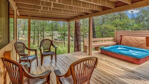 Een houten terras met een jacuzzi, stoelen en uitzicht op een bos.