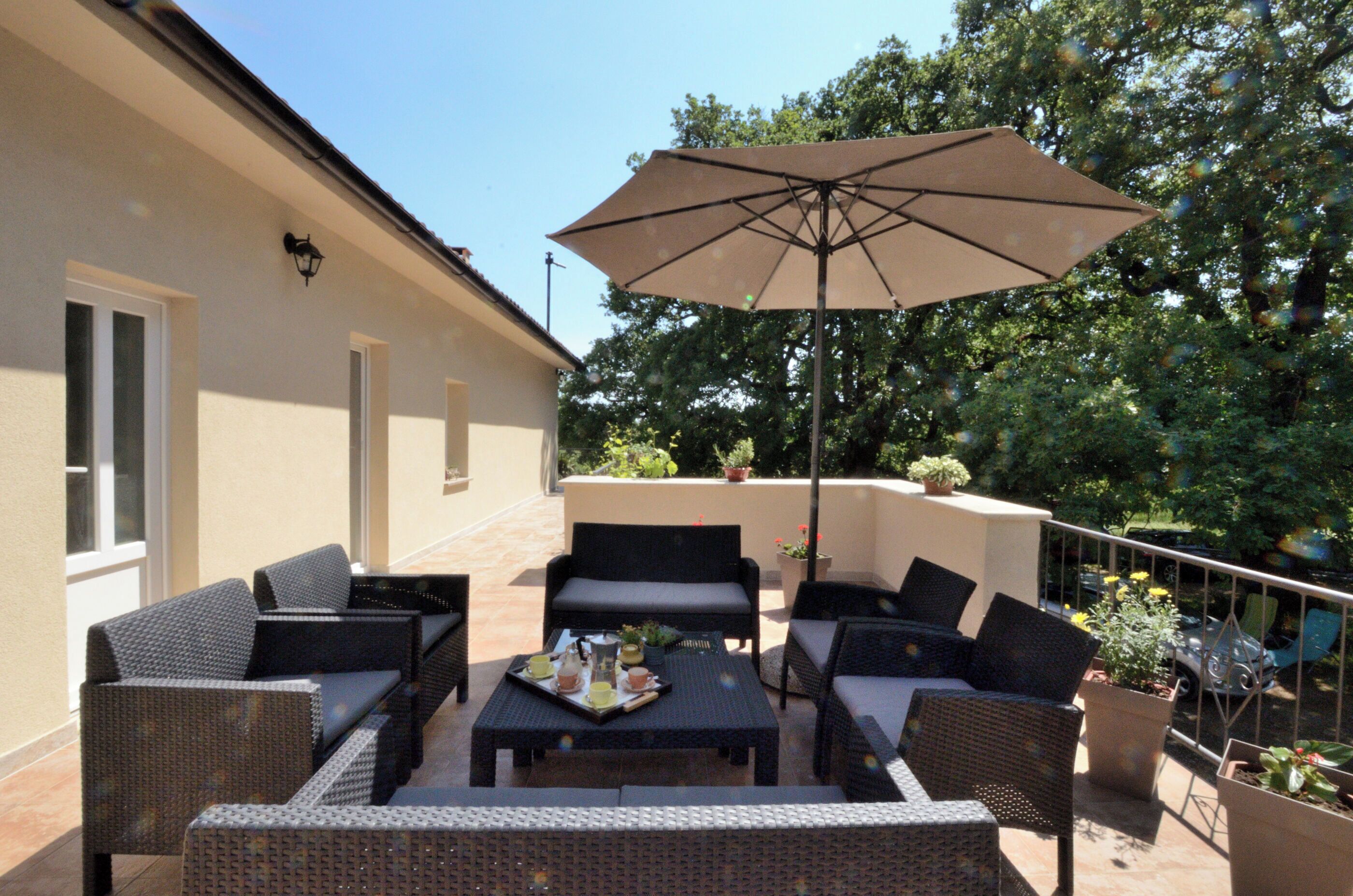 An outdoor patio with wicker furniture, a table with a tray of drinks, and an umbrella.