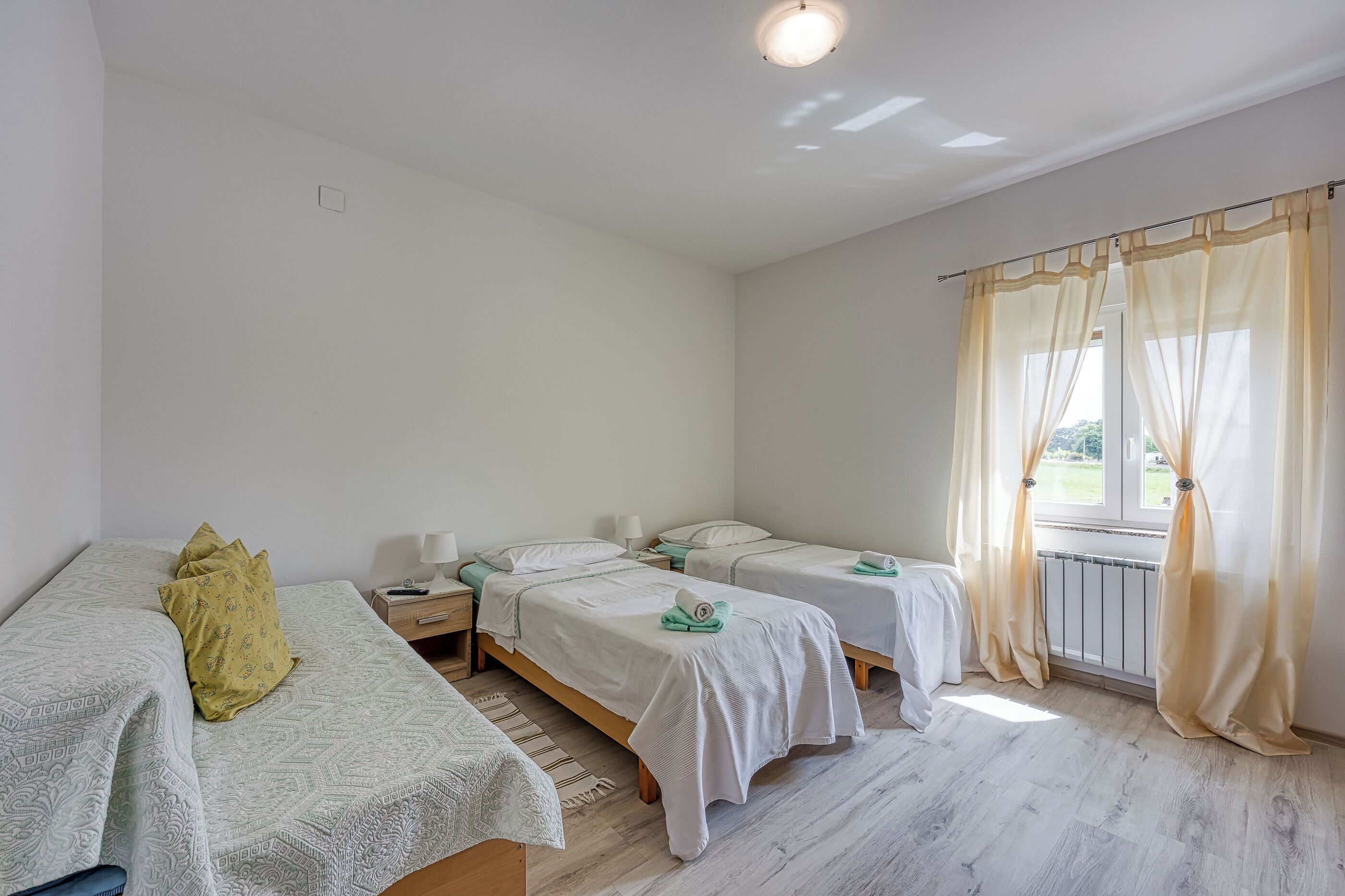 A room with two single beds, a nightstand, a lamp, and a window with curtains.