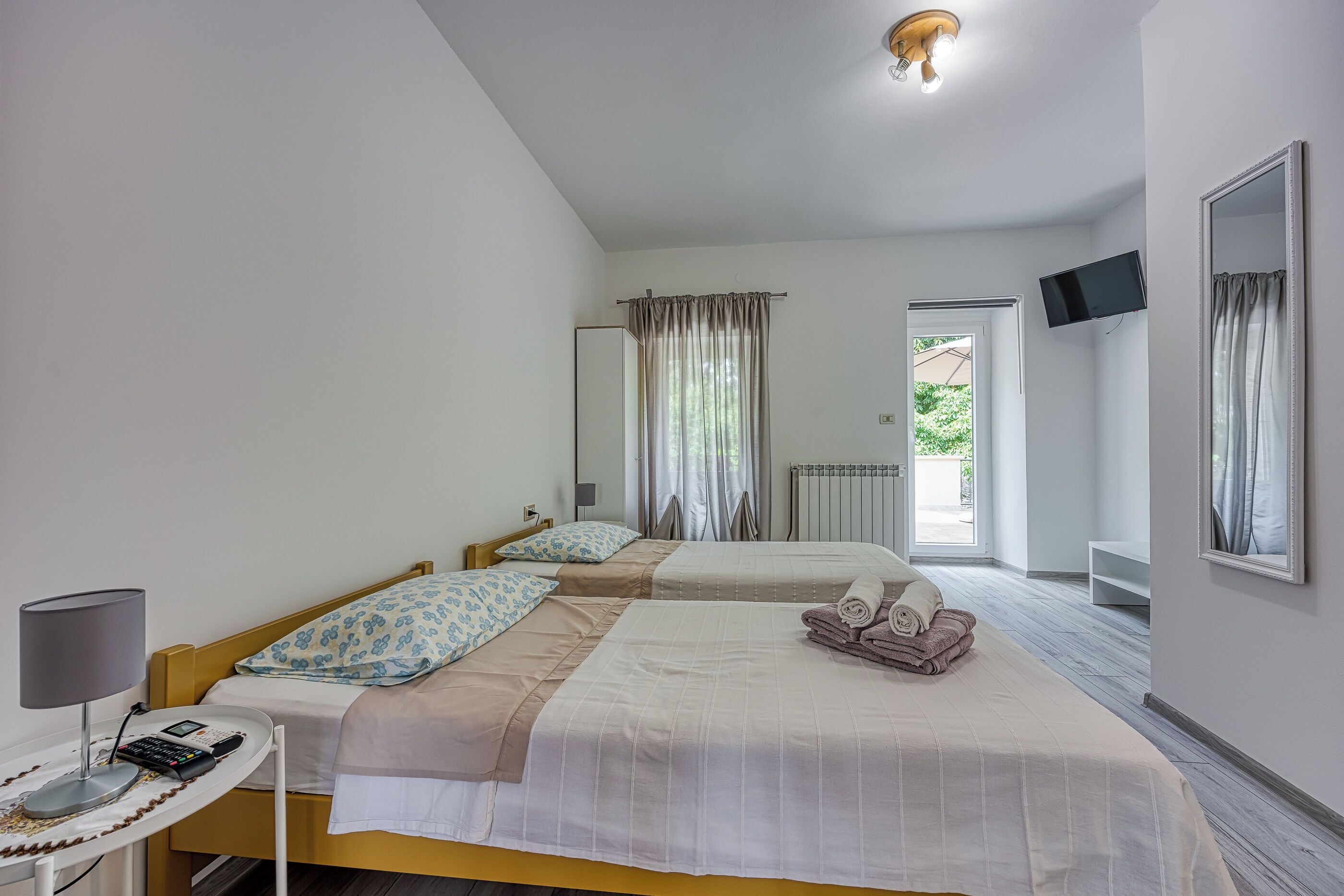 Habitación de hotel con dos camas, televisión, escritorio con lámpara y ventana con cortinas.