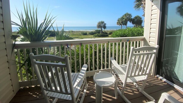 A balcony with white chairs and a small table, overlooking a beach with palm trees and the ocean. - Ocean Forest Villas by Palmetto Vacations (Myrtle Beach)