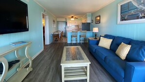 A living room with a blue sofa, a coffee table, and a TV on a stand. - Ocean Forest Villas by Palmetto Vacations (Myrtle Beach)